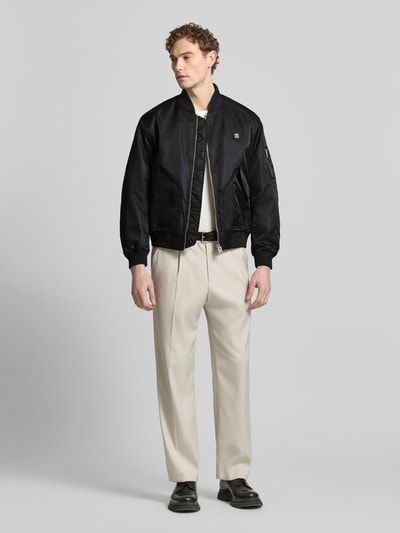 Männermodel trägt Regular Fit Bomberjacke mit Label-Applikation Modell 'Badam2611' von HUGO in Schwarz, Twill, Ganzkörperansicht von vorne.