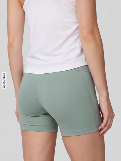 Frauenmodel trägt Eng anliegende Sportshorts mit Logo-Print Modell 'Tempo' von Nike, sanftes Grün, glatte Textur, Ganzkörperansicht Rückansicht, Damen Sportshorts von Nike Training, KI-modifiziertes Bild.