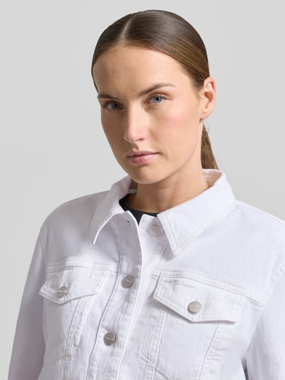 Kobiece modelka nosi Jeansjacke mit Brusttasche und Fransen od Marc Cain, biały kolor, krój slim fit, bawełna z elastanem, zapięcie na guziki, kieszenie na piersi, długość tyłu w rozmiarze 36: 47 cm, szerokość ramion w rozmiarze 36: 39 cm, szerokość w rozmiarze 36: 37 cm, długość rękawa w rozmiarze 36: 59 cm, zbliżenie na górną część ciała