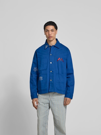 Männermodel trägt Hemdjacke mit Motiv-Stitching von Forét in Blau aus Baumwoll-Mix, Relaxed-Fit, aufgesetzte Taschen, durchgängige Knopfleiste, Rückenlänge 73 cm bei Größe M, Ganzkörperansicht von vorne.