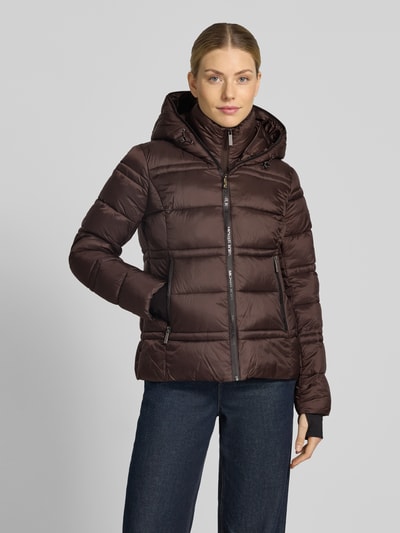 Frauenmodel trägt Steppjacke mit Kapuze und Reißverschlusstaschen von MICHAEL Michael Kors in Braun, glatte Textur, seitliche Taschen, Ganzkörperansicht von vorne.