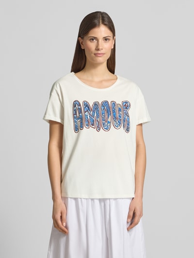 Kobiece model prezentuje damski t-shirt z obszyciem z kamieni stras Oui, kolor biały, prosty krój, dekolt w łódkę, długość tyłu 60 cm w rozmiarze 36, materiał: bawełna, widok całej sylwetki z przodu.