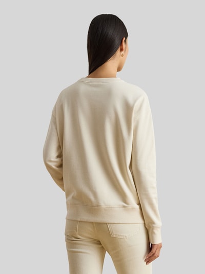 Modelka kobieca nosi Regular Fit Sweatshirt aus Baumwoll-Mix od Lauren Ralph Lauren, gładki kremowy krój regular fit, detal z nadrukiem logo, okrągły dekolt, długie rękawy, prążkowane wykończenia, materiał bawełna-mix, widok całej sylwetki z tyłu.