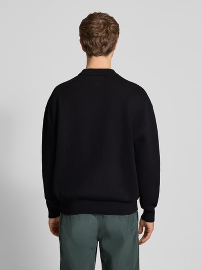 Männermodel trägt Strickpullover mit Label-Detail von BLKVIS in Schwarz, reine Baumwolle, lockerer Schnitt, gerippte Abschlüsse, Rundhalsausschnitt, Rückenlänge 68 cm, Ärmellänge 60 cm, Ganzkörperansicht Rückansicht.