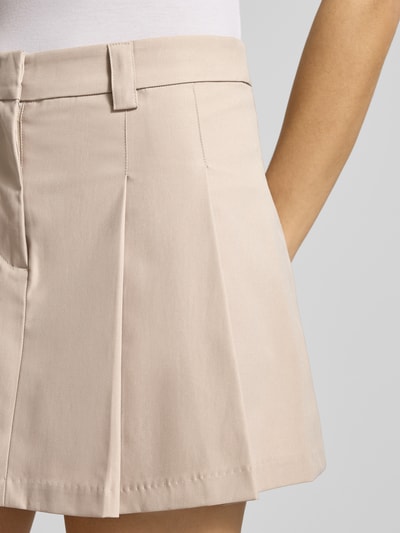 Frauenmodel trägt Faltenrock in A-Linie von Gina Tricot, beige, strukturierte Oberfläche, Bundweite 39 cm, Gesamtlänge 37 cm, Nahaufnahme Oberkörper.