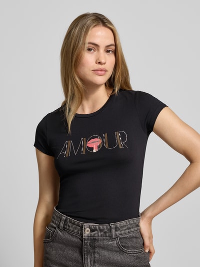 Vrouwenmodel draagt T-shirt met Ziersteinbesatz van Guess in zwart, slim fit, mix van katoen en elastaan, ronde hals, ruglengte 65 cm, nahaufnahme bovenlichaam.