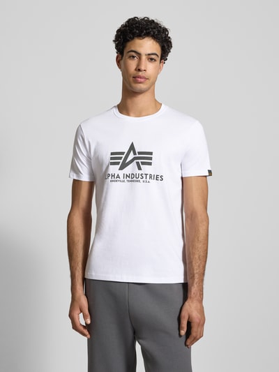 Męski model nosi T-Shirt mit Label-Print od Alpha Industries, biały kolor, prosty krój, okrągły dekolt, bawełna, całkowity przód.