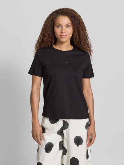Kobiece modelka nosi Regular Fit T-Shirt aus reiner Baumwolle von Marc O'Polo Denim, czarny, krój regular fit, gładki jersey, nadruk z logo, krótkie rękawy, widok całej sylwetki z przodu.