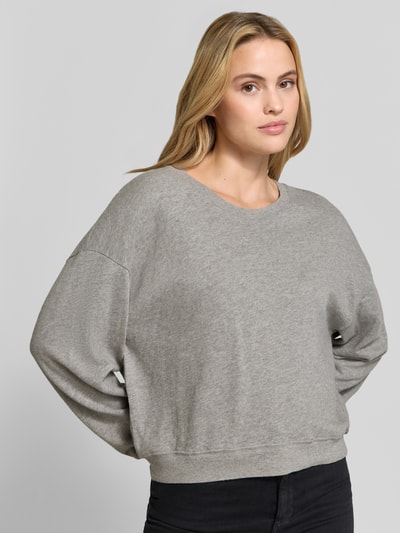 Frauenmodel trägt Sweatshirt mit überschnittenen Ärmeln Modell 'SONOMA' von American Vintage, reine Baumwolle, lockerer Schnitt, Rundhalsausschnitt, graue Textur, Ganzkörperansicht von vorne.
