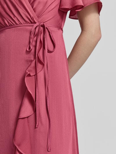 Frauenmodel trägt Abendkleid in Wickel-Optik mit Bindegürtel von Christian Berg Cocktail aus rosafarbenem Satin, taillierter Schnitt, Volantsaum, Nahaufnahme Oberkörper.
