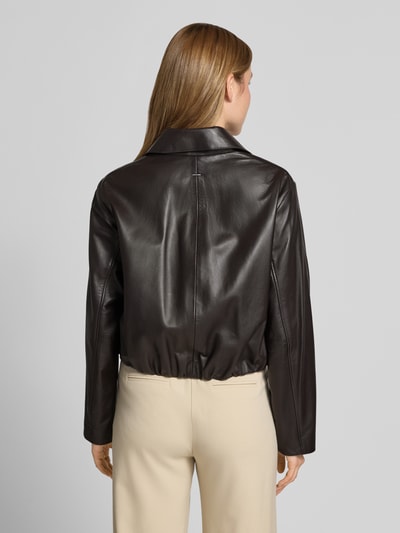 Frauenmodel trägt Regular Fit Lederjacke aus echtem Lammleder Modell 'SARCAE' von BOSS, mattschwarze Lederoptik, elastische Bündchen, Reverskragen, Druckknopfleiste, seitliche Taschen, Ganzkörperansicht Rückansicht.