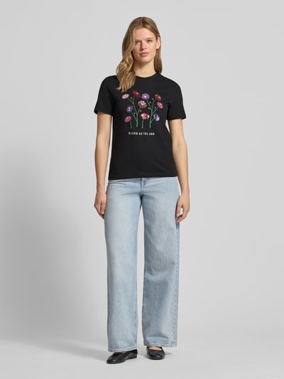 Frauenmodel trägt Damen T-Shirt Slim Fit T-Shirt aus reiner Baumwolle Modell 'KITA' von Only, Optik: Unifarben, Motiv-Print mit Pailletten, Rundhals, Kurzarm, Jersey, reine Baumwolle, schwarze Farbe mit floralen Details, Ganzkörperansicht von vorne.