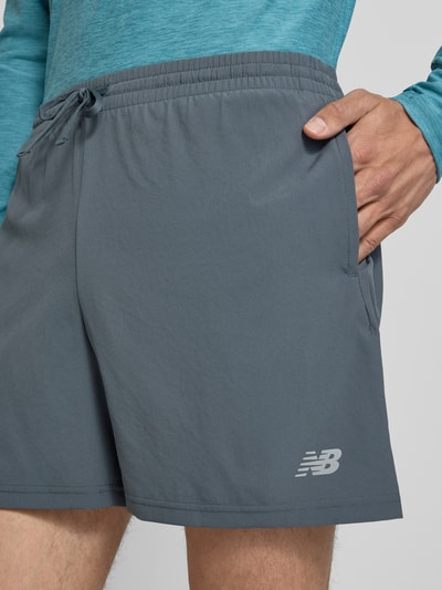 Männermodel trägt Shorts mit elastischem Bund und Logo von New Balance in Grau, Regular-Fit, Tunnelzug, Logo-Print, Nahaufnahme Oberschenkel.