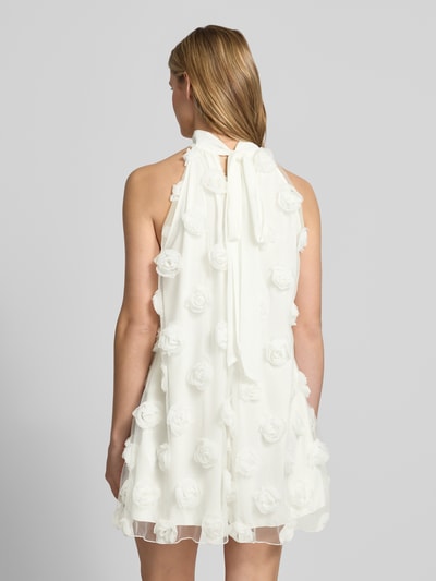 Frauenmodel trägt Minikleid mit floralen Applikationen von Gina Tricot, Loose-Fit, Neckholder, weiß, strukturierte Oberfläche, Rückenlänge 83 cm, Brustweite 57 cm, Schlüsselloch-Ausschnitt, Ganzkörperansicht Rückansicht.