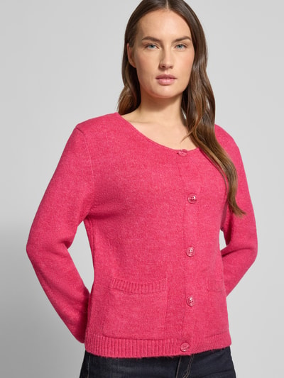 Vrouwenmodel draagt Strickjacke mit Knopfleiste van More & More in felroze, regular fit, geribde boorden, voorkant, close-up bovenlichaam.