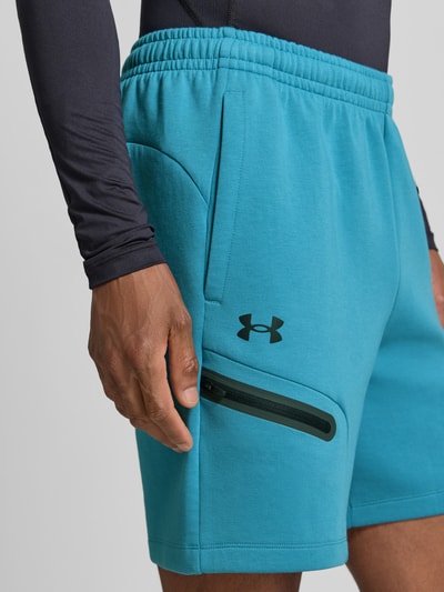 Mężczyznamodel nosi szorty z kieszenią zapinaną na zamek błyskawiczny Under Armour, mieszanka bawełny, krój regular fit, logo, elastyczny pas; szerokość w rozmiarze M: 39 cm, długość wewnętrzna nogawki w rozmiarze M: 18 cm, zbliżenie na górną część nogawki z przodu.
