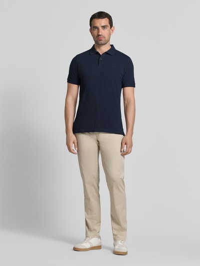 Männermodel trägt Regular Fit Poloshirt aus reiner Baumwolle von s.Oliver RED LABEL in Dunkelblau, helle Hose, Ganzkörperansicht von vorne.