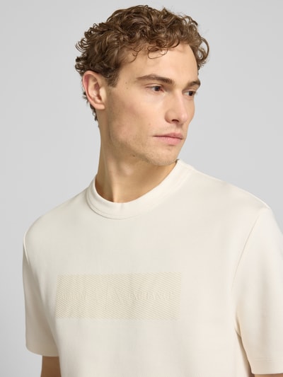 Männermodel trägt T-Shirt mit Logo und Rundhalsausschnitt von ARMANI EXCHANGE in Creme, Reine Baumwolle, Regular-Fit, Nahaufnahme Oberkörper. Rückenlänge bei Größe M: 71 cm.