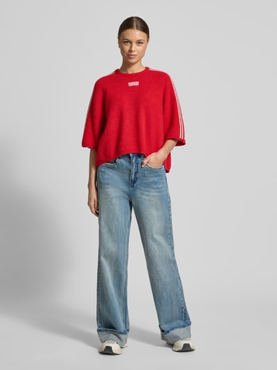 Frauenmodel trägt Cropped Strickpullover mit gerippten Abschlüssen Modell 'VITOW' von American Vintage in Rot, lockerer Schnitt, Rundhalsausschnitt, Woll-Alpaka-Mix mit Stretch, Label-Stitching, kombiniert mit blauen Jeans, Ganzkörperansicht von vorne.