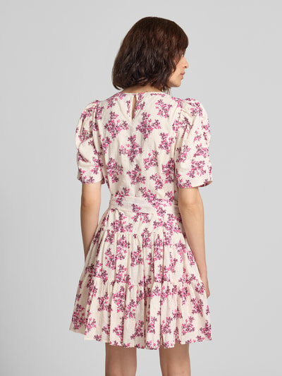 Frauenmodel trägt Minikleid im Allover-Look mit Bindegürtel von Neo Noir aus reiner Baumwolle, florales Muster, Detail Annitas Starling Flower, A-Linie, Rundhalsausschnitt, helle Grundfarbe mit pinken Blumen, Ganzkörperansicht Rückansicht.