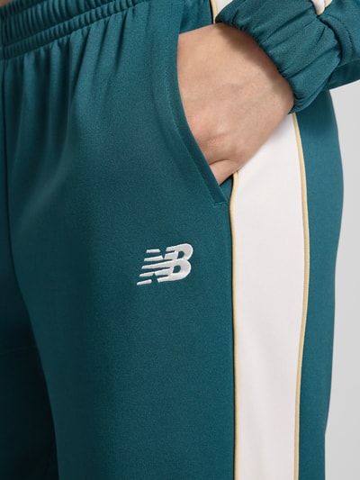 Frauenmodel trägt Sweatpants mit elastischem Bund und Label-Stitching von New Balance in Türkis mit weißen Kontraststreifen, Relaxed-Fit, Eingrifftaschen, Detailaufnahme, Innenbeinlänge bei Größe S 80 cm.