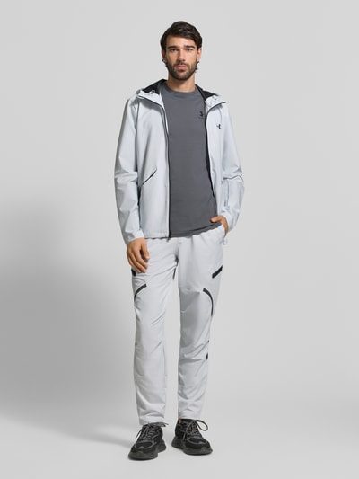 Męski model trägt Regular Fit T-Shirt mit Logo-Print Modell 'Left' von Under Armour, mieszanka bawełny, okrągły dekolt, długość tyłu 72 cm w rozmiarze M, Ganzkörperansicht von vorne.