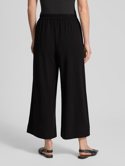 Frauenmodel trägt schwarze Stoffhose in verkürzter Passform Modell 'Coralie' von MAC, lockerer Schnitt, elastischer Bund, Ganzkörperansicht Rückansicht.