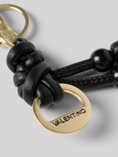 Produktfoto, Schlüsselanhänger mit Ziersteinbesatz Modell 'Eloura' von VALENTINO BAGS, goldfarbene Details, schwarze Lederschlaufen, glänzende Oberfläche, Logo-Detail, neutraler Hintergrund.