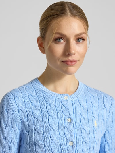 Vrouwenmodel draagt Regular Fit Strickjacke aus reiner Baumwolle van Polo Ralph Lauren in effen blauw kabelbreisel, logo-stiksel, ronde hals, lange mouw, geribde afwerking, materiaal katoen. Close-up bovenlichaam.