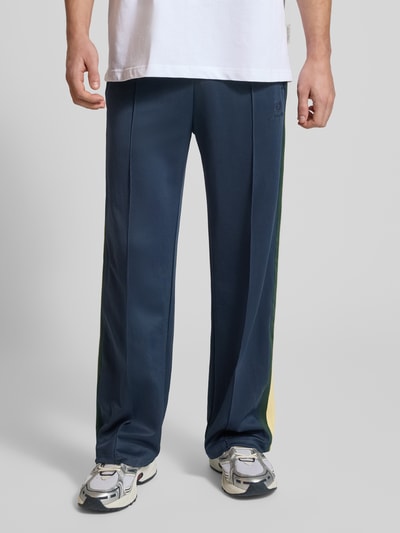 Männermodel trägt Track Pants mit Reißverschlusstaschen und Kordelzug von ANOTHER COTTON LAB, weites Bein, elastischer Bund, Ganzkörperansicht von vorne