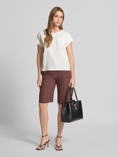 Frauenmodel trägt Blusenshirt mit verlängertem Rücken und Brusttasche von monari in Creme mit Rundhalsausschnitt, Aufschlag und Label-Detail, Gerader-Schnitt, Ganzkörperansicht von vorne.