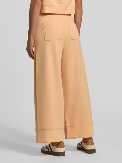 Frauenmodel trägt Wide Leg Sweatpants aus Modal-Mix von Rich & Royal in Pfirsichfarbe mit Bundfalten und Gesäßtaschen, Ganzkörperansicht Rückansicht.