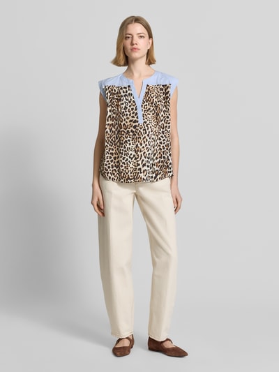 Frauenmodel trägt Relaxed Fit Bluse aus reiner Viskose mit Allover-Animal-Print von Emily Van den Bergh, Tunika-Ausschnitt, ärmellos, beige-braun gemustert, blaue Akzente, Ganzkörperansicht von vorne.