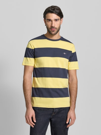 Männermodel trägt Regular Fit T-Shirt mit Logo-Print Modell 'BAR' von Gant in Gelb und Dunkelblau, reine Baumwolle, Ganzkörperansicht von vorne.