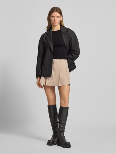 Kobiece model prezentuje Slim Fit Langarmshirt aus Baumwoll-Mix od Tommy Jeans w czarno-beżowe paski, drobne logo, materiał prążkowany, długie rękawy z falbankami, widok całej sylwetki z przodu.