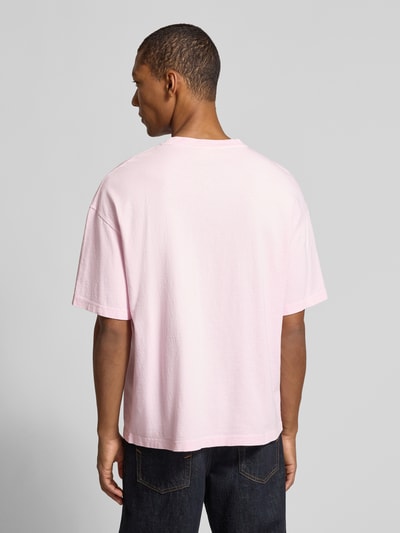 Männermodel trägt T-Shirt aus reiner Baumwolle mit Brusttasche Modell 'AFOMA' von American Vintage in Hellrosa, Ganzkörperansicht Rückansicht. Relaxed Fit, Halbarm, Rundhalsausschnitt, überschnittene Schultern, Rückenlänge bei Größe M 70 cm.