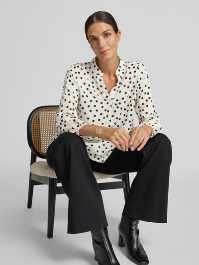 Frauenmodel trägt Relaxed Fit Bluse aus reiner Viskose-Mix Modell 'Valeria' von ZABAIONE, weiße Bluse mit schwarzen Punkten, Langarm, Serafino Ausschnitt, kombiniert mit schwarzer Hose, Ganzkörperansicht von vorne, Damen Bluse Relaxed Fit, Rückenlänge 54 cm, Ärmellänge 58 cm.