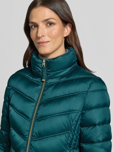 Kobieta prezentuje Steppmantel mit Zweiwege-Reißverschluss von Christian Berg Woman Selection w zielonym kolorze, tekstura pikowana, krój slim fit, kaptur z troczkiem, kieszenie na zamek, długość tyłu 83 cm, szerokość ramion 40 cm, szerokość w biuście 48 cm, długość rękawa 65 cm, zbliżenie na górną część ciała.