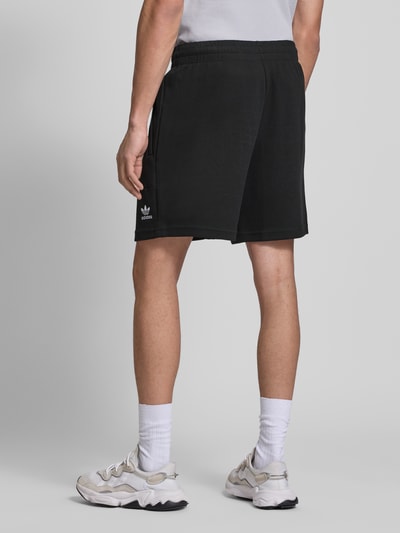 Männermodel trägt Relaxed Fit Sweatshorts mit Baumwoll-Anteil von adidas Originals in Schwarz, Waffelstruktur, Logo-Stitching, Rückansicht.