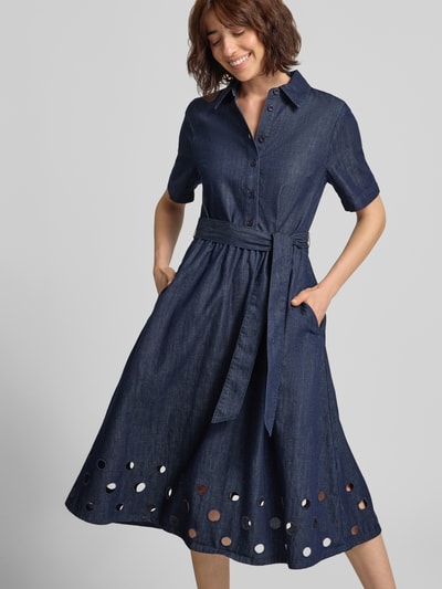 Frauenmodel trägt Hemdblusenkleid in Denim-Optik mit Bindegürtel von MORE & MORE, reine Baumwolle, Lochstickerei, A-Linie, Midikleid, Hemdblusenkragen, Knopfleiste, dunkelblauer Farbton, glatte Textur, Ganzkörperansicht von vorne.