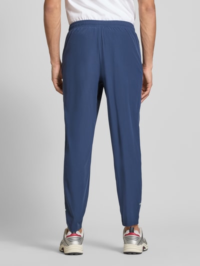 Mężczyzna nosi Trackpants mit elastischem Bund Modell 'EVARO' von Ellesse, materiał ze stretchem, krój regular fit, kolor niebieski, gładka tekstura, widok całej sylwetki z tyłu, długość nogawki w rozmiarze M: 74 cm.