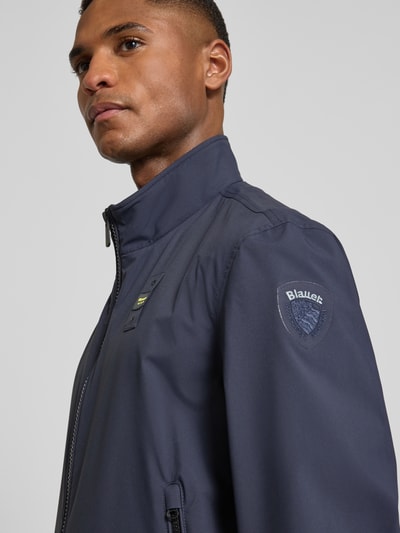 Männermodel trägt Jacke mit Label-Patches Modell 'Anson' von Blauer Usa in Dunkelblau, glatte Struktur, Nahaufnahme Oberkörper.