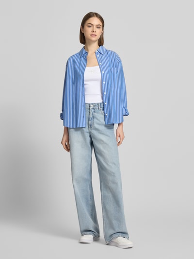Kobiece modelka nosi Slim Fit Top mit Logo-Print Modell 'Scoop' od Calvin Klein Jeans, krój slim fit, okrągły dekolt, długość pleców w rozmiarze S: 42 cm, jasne kolory i tekstura bawełny, pełny widok z przodu.