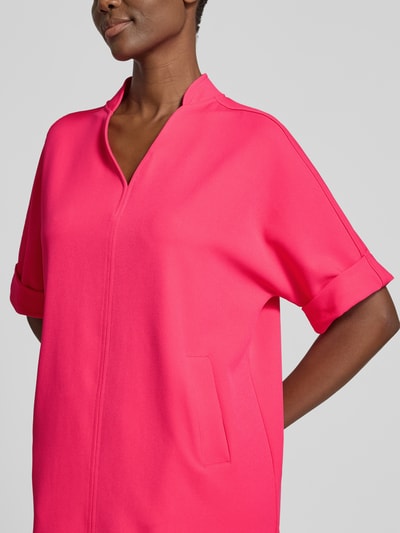Frauenmodel trägt Knielanges Kleid mit Eingrifftaschen von Milano Italy in kräftigem Pink, Material-Mix mit Stretch-Anteil, gerader Schnitt, Stehkragen, V-Ausschnitt, 1/2-Arm mit Aufschlag, strukturierte Oberfläche, Nahaufnahme Oberkörper.
