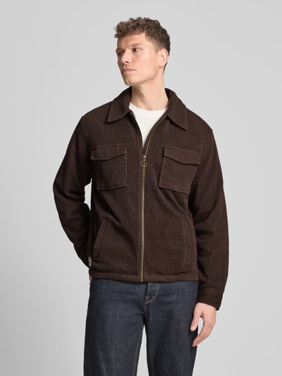 Męski model nosi Regular Fit Hemdjacke mit Strukturmuster od Scotch & Soda, bawełna, krój regular fit, brązowy kolor, tekstura, kieszenie, zamek, widok całej sylwetki z przodu.
