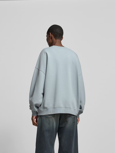 Männermodel trägt Oversized Sweatshirt aus reiner Baumwolle von Anine Bing in hellem Grau, lockerer Sitz, elastische Abschlüsse, Rückenlänge 64 cm, Ganzkörperansicht Rückansicht.