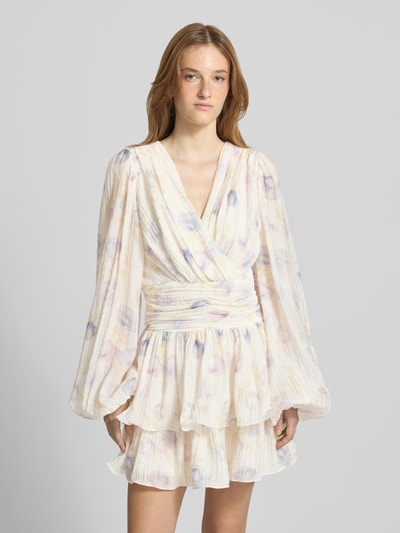 Frauenmodel trägt Minikleid aus Viskose-Mix mit V-Ausschnitt von Gina Tricot, floraler Allover-Print, langärmelig, Tailliert, Raffung, zarte Pastellfarben, weiche Textur, Ganzkörperansicht von vorne. Rückenlänge 84 cm, Brustweite 42 cm, Ärmellänge 70 cm.