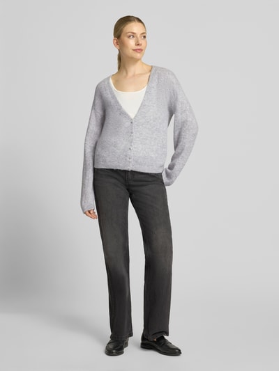 Frauenmodel trägt Relaxe-Fit Strickjacke aus Alpacka-Mix mit Woll-Anteil Modell 'C_Farano' von BOSS Orange, meliertes Hellgrau, gerippte Abschlüsse, Knopfleiste, V-Ausschnitt, Ganzkörperansicht von vorne.