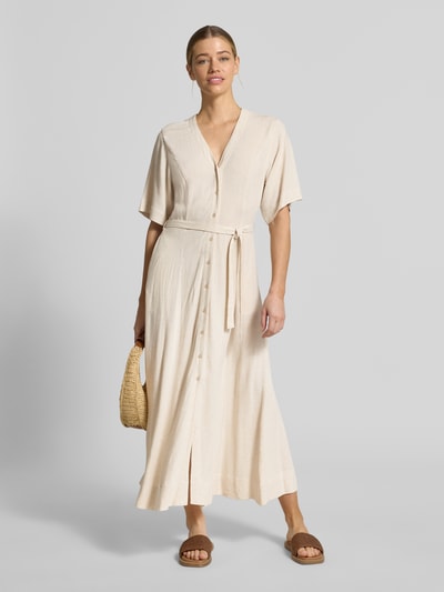 Kobiece modelka nosi Regular Fit Leinenkleid mit V-Ausschnitt Modell 'VIVA' von Selected Femme z lnu i wiskozy, jasny beż, maxi, krój regular fit, jednolity, guziki, pasek, kieszenie boczne, widok całej sylwetki z przodu.