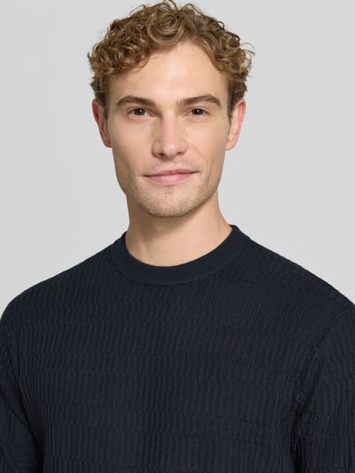 Männermodel trägt Slim Fit Strickshirt aus reiner Wolle von Emporio Armani in Dunkelblau, gerippte Textur, Nahaufnahme Oberkörper.